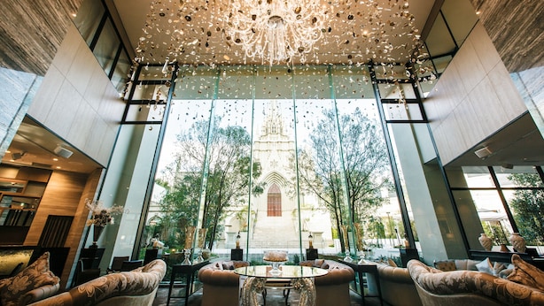 A spacious lobby with a large chandelier, comfortable seating, and a view of a building with a tower. - The Strings Hotel Nagoya (Nagoya)