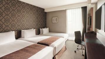 A hotel room with two beds, a desk, a chair, a television, and a patterned wall.