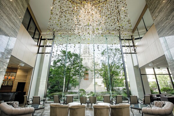 A spacious lobby with a large chandelier, comfortable seating, and large windows offering a view of a building and greenery outside. - The Strings Hotel Nagoya (Nagoya)