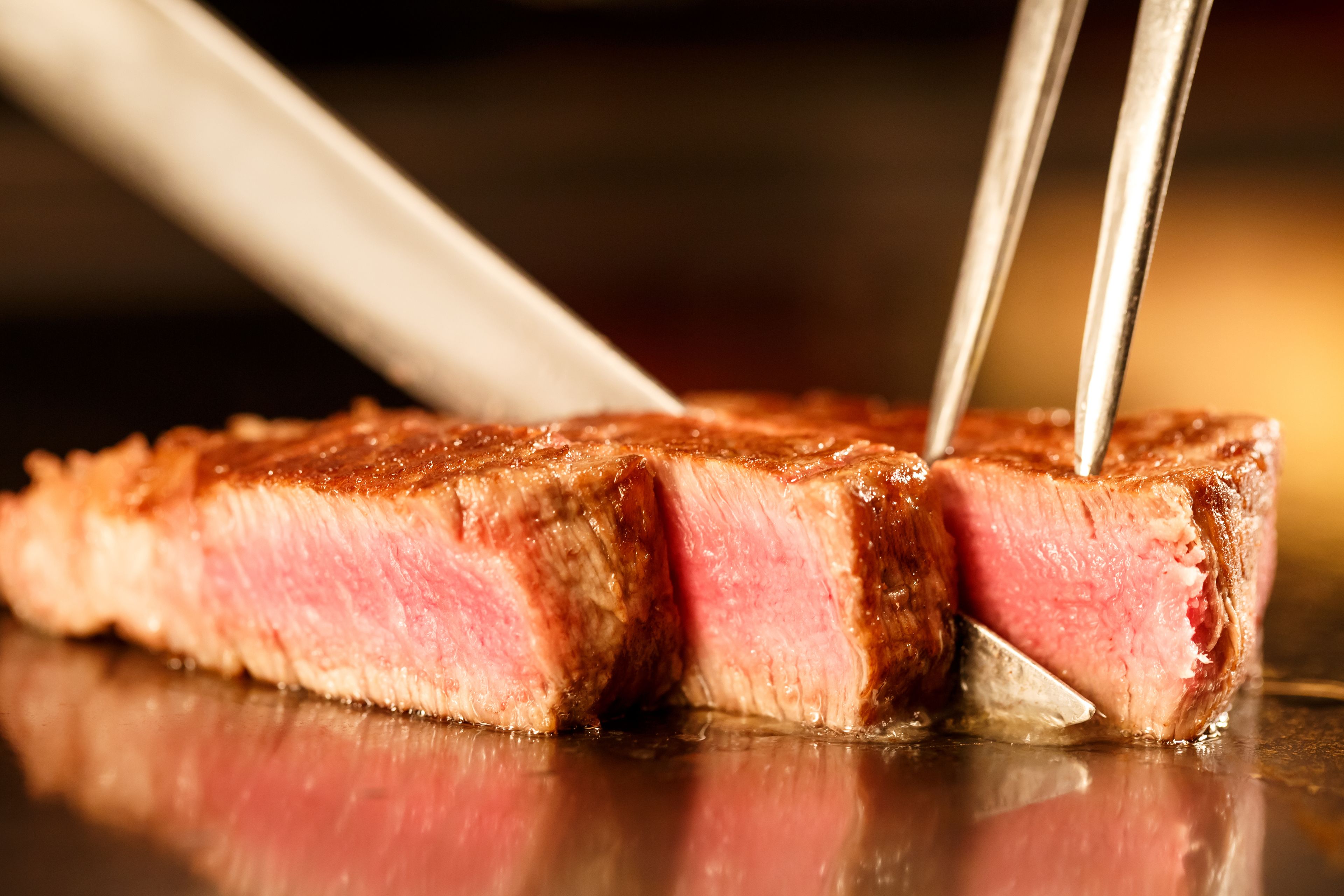 A close-up of a steak being cut with tongs.