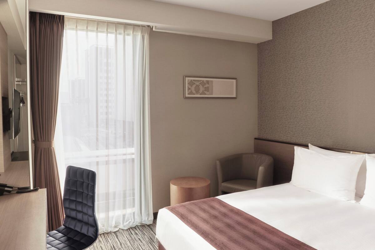 Hotellihuone, jossa on sänky, tuoli, työpöytä ja televisio.