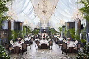 Un comedor formal con varias mesas, candelabros elegantes y abundante vegetación.