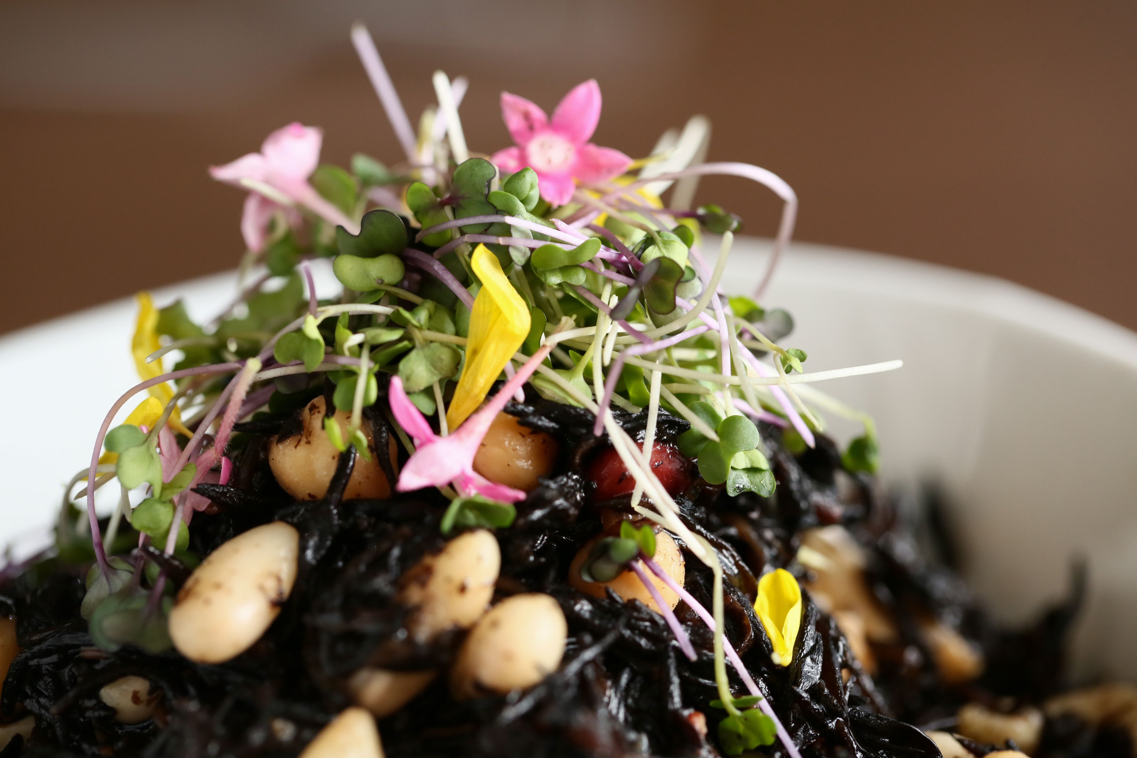 A bowl of salad with various greens, chickpeas, and flowers.