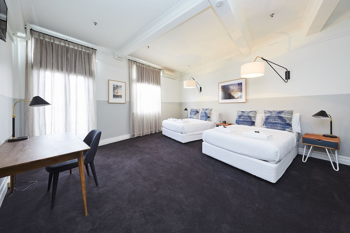 A hotel room with two beds, a desk, a chair, and a table.