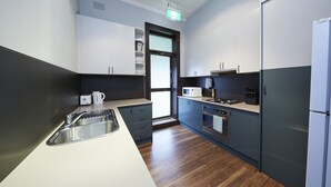 A modern kitchen with a stainless steel sink, white cabinets, a microwave, and a built-in oven. - Bridgeview Hotel Willoughby (Willoughby)