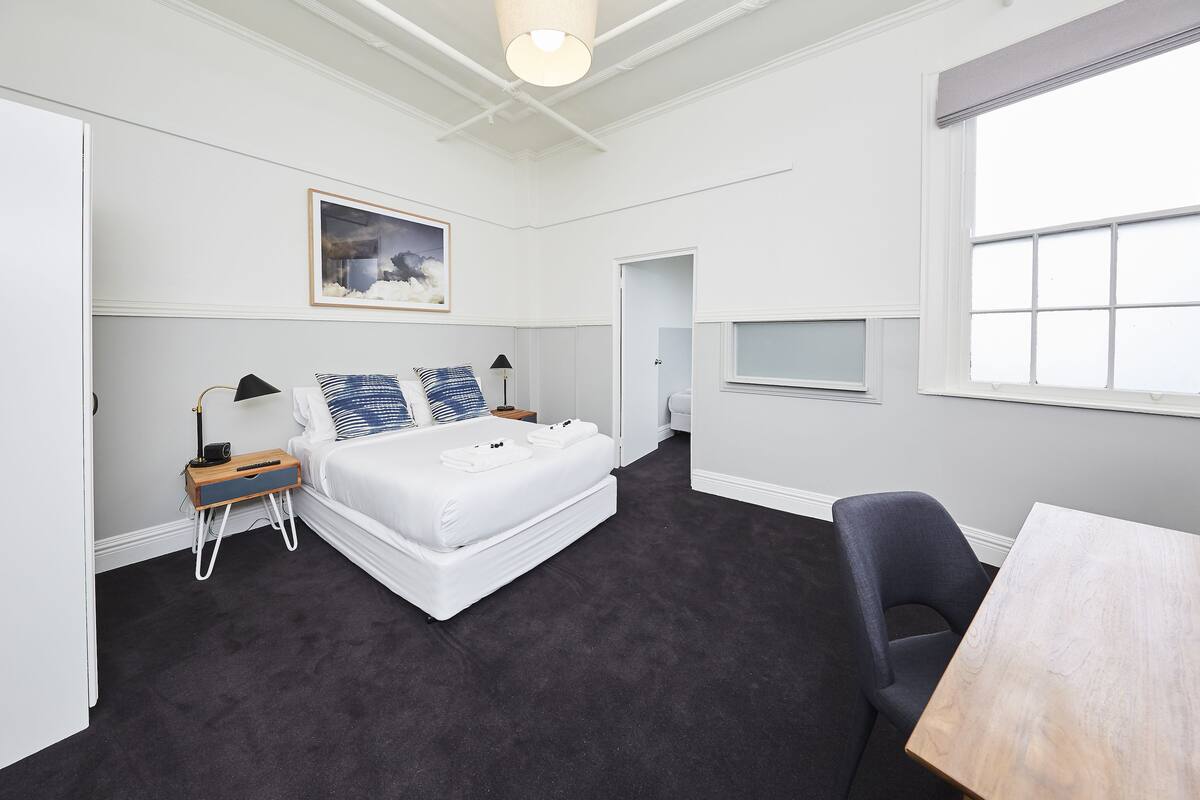 A hotel room with a bed, bedside table, lamp, and a small window.