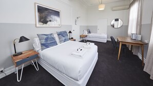 A hotel room with a large bed, bedside tables, a desk, a chair, a mirror, and a painting on the wall. - Bridgeview Hotel Willoughby (Willoughby)