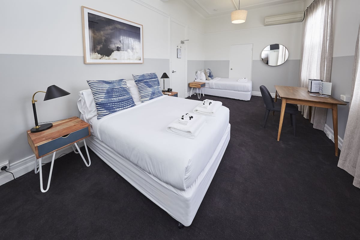 A hotel room with a large bed, bedside tables, a desk, a chair, a mirror, and a painting on the wall.