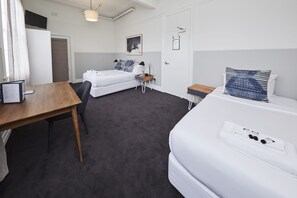 A hotel room with two beds, a desk, a chair, a small table, a TV, and a framed picture on the wall. - Bridgeview Hotel Willoughby (Willoughby)