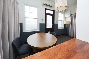 A conference room with a wooden table, two chairs, a door with a sign, windows, and an air conditioning unit. - Bridgeview Hotel Willoughby (Willoughby)