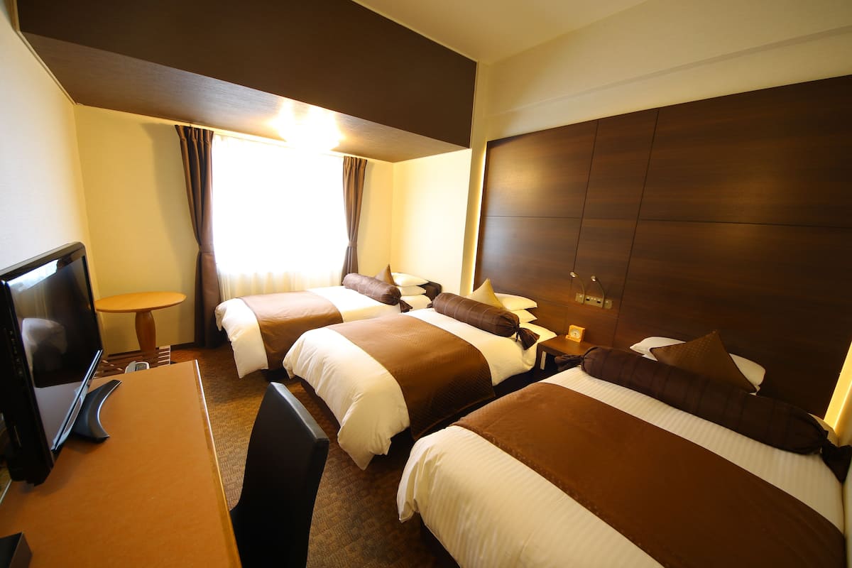 Habitación de hotel con tres camas, un escritorio y una televisión.