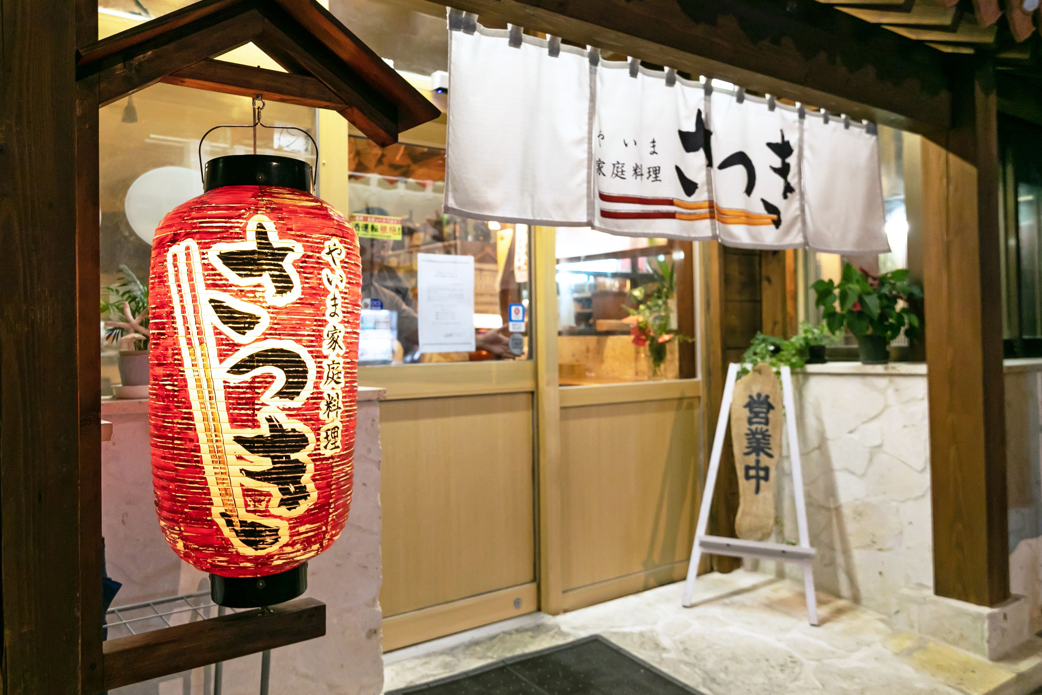 Perinteinen japanilainen lyhty, jossa on kiinalaisia kirjoitusmerkkejä, puinen sisäänkäynti ja kyltti, jossa on japanilaisia kirjoitusmerkkejä.