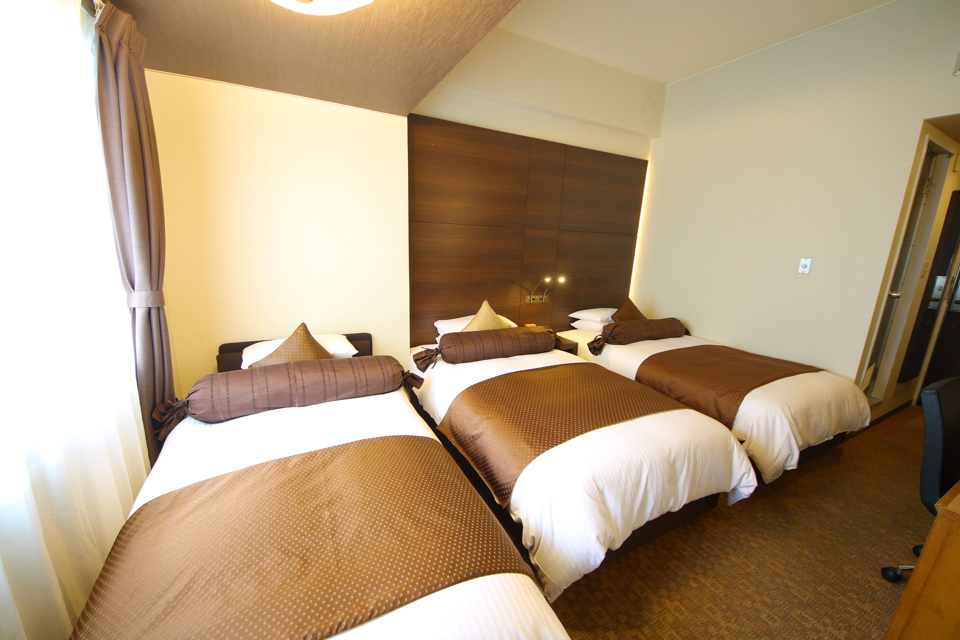 A hotel room with three single beds, each with brown and white bedding.