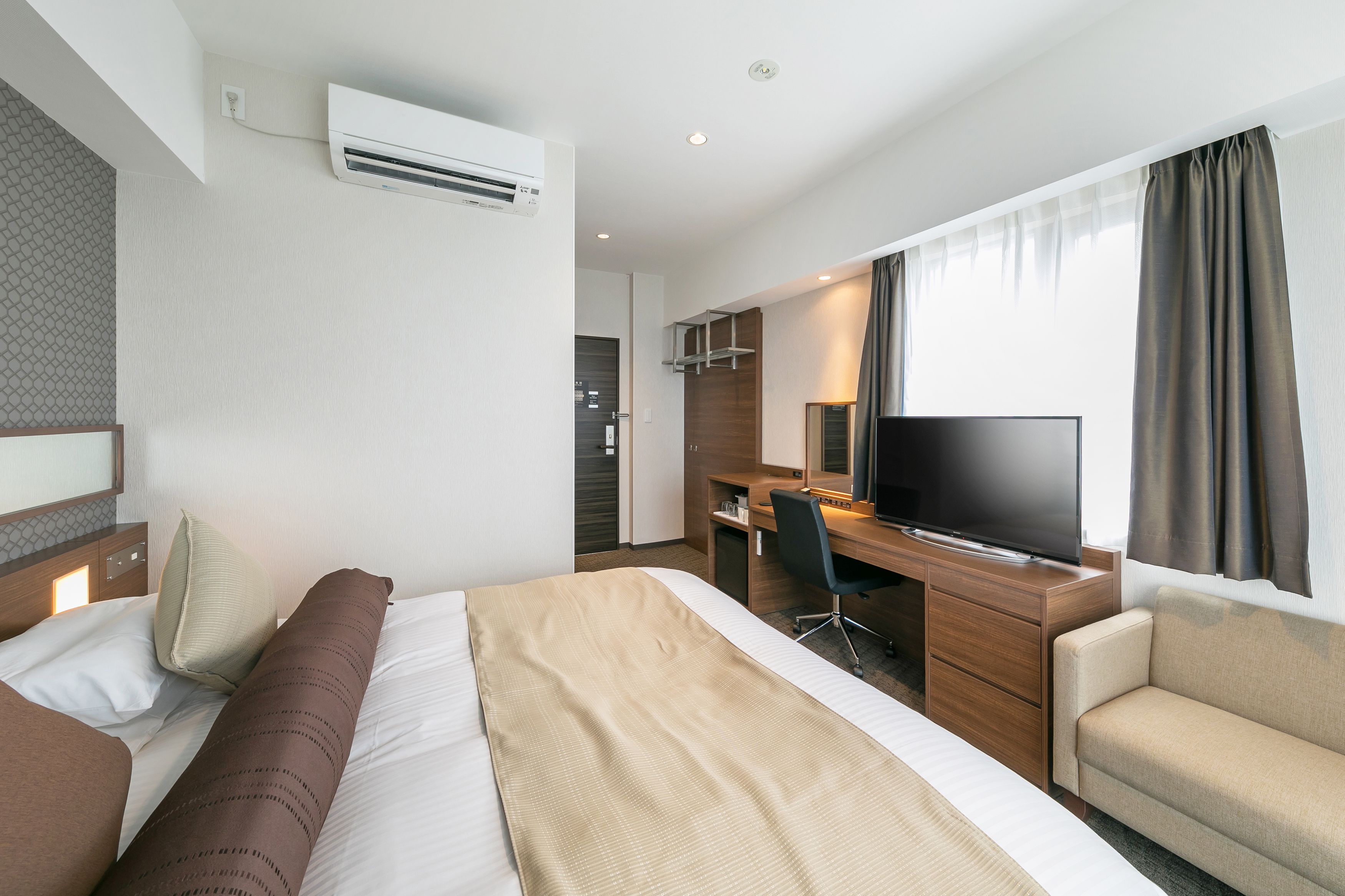 Una habitación de hotel con cama, sofá, escritorio con televisor y armario.