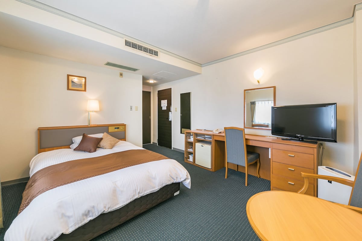 Habitación de hotel con cama, escritorio, silla, televisor y refrigerador pequeño.