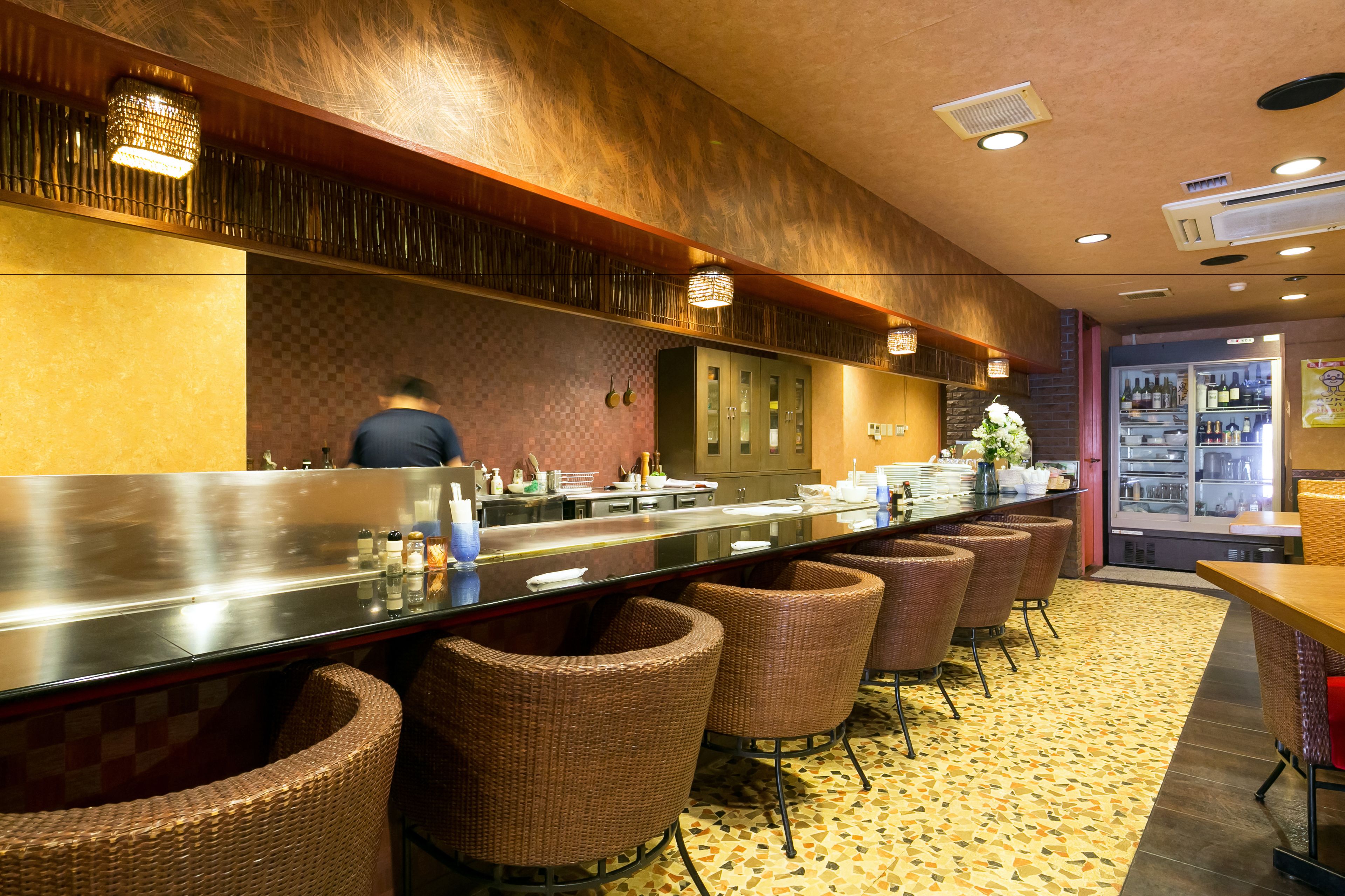 A long bar area with wicker chairs, a stainless steel counter, and a refrigerator stocked with bottles.