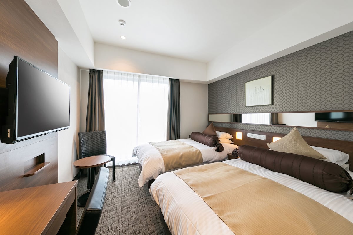 Habitación de hotel con dos camas, televisión, escritorio y ventana con cortinas.