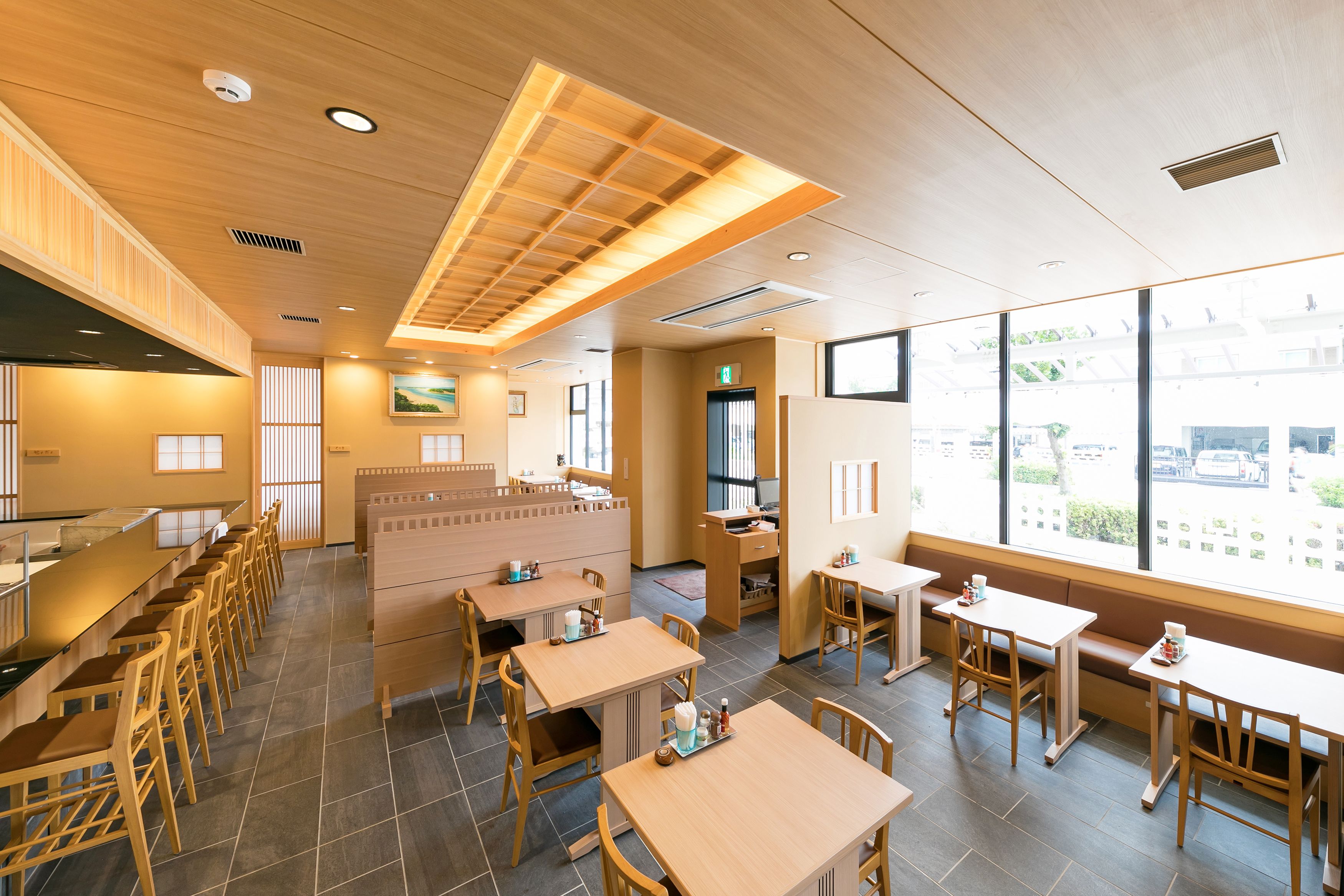 A modern restaurant interior with wooden furniture, large windows, and a central seating area.