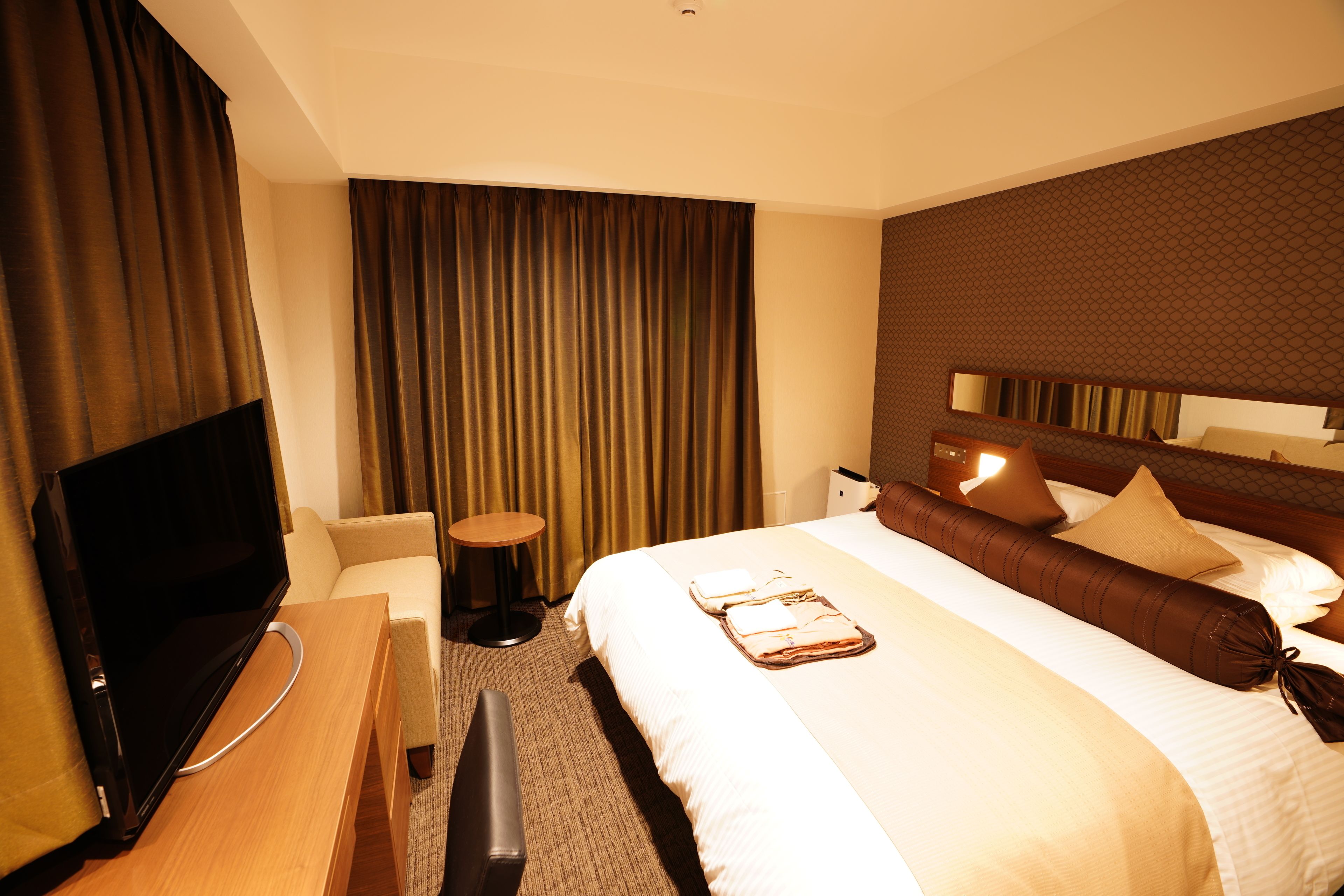 A hotel room with a bed, a TV, a desk, and a chair.