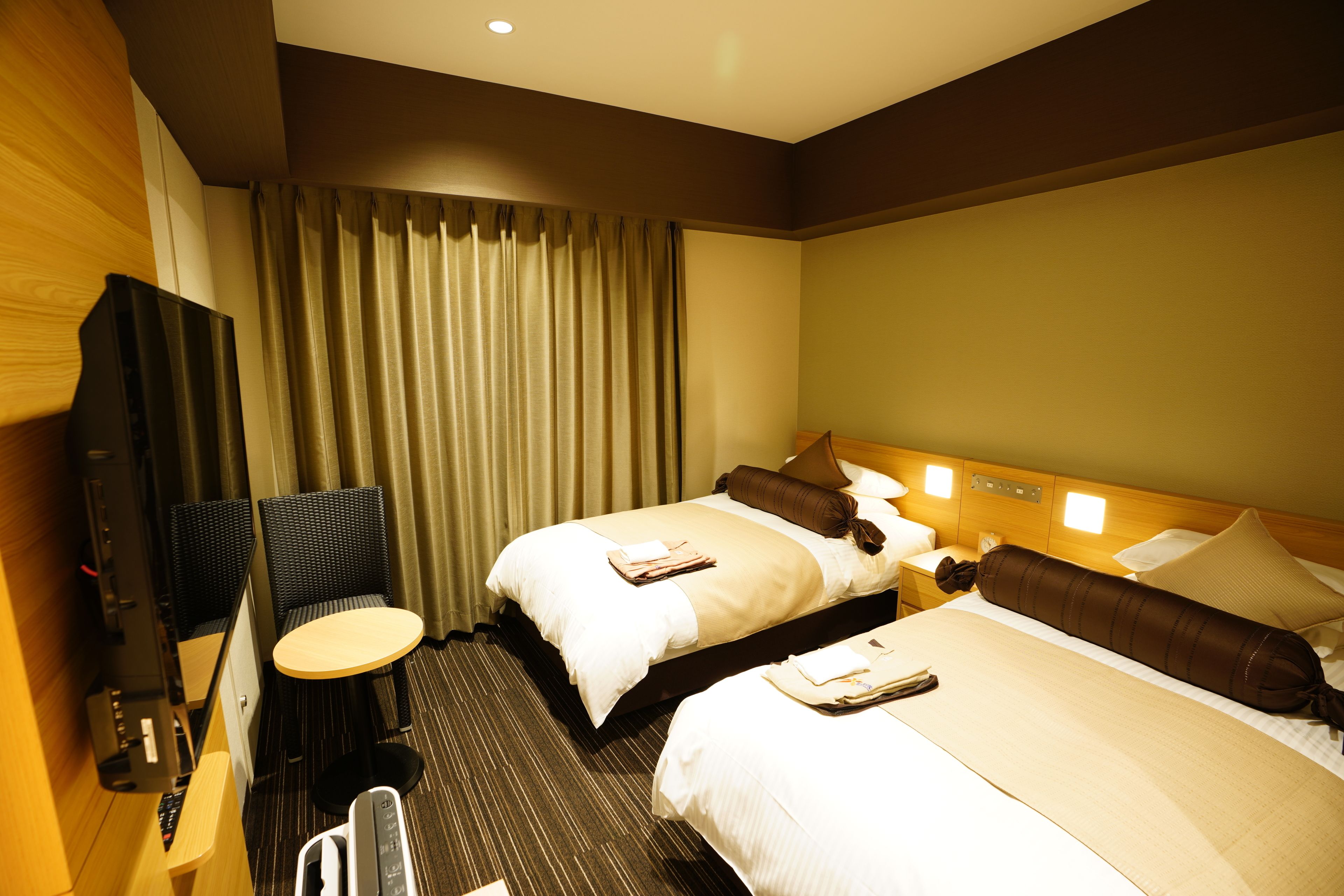 A hotel room with two beds, a desk, a chair, a TV, and a window with curtains.