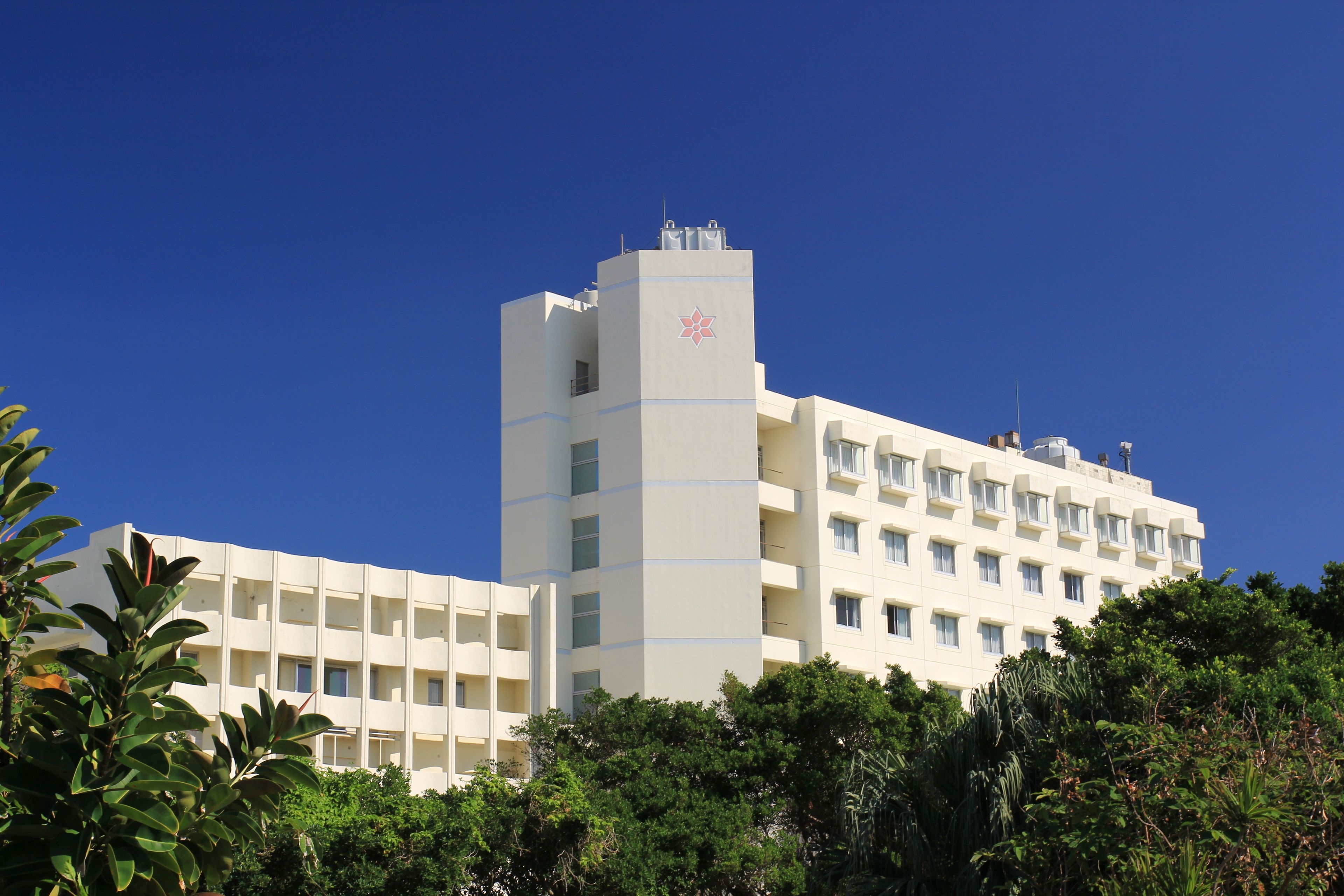 A multi-story hotel with a prominent central tower, surrounded by lush greenery.