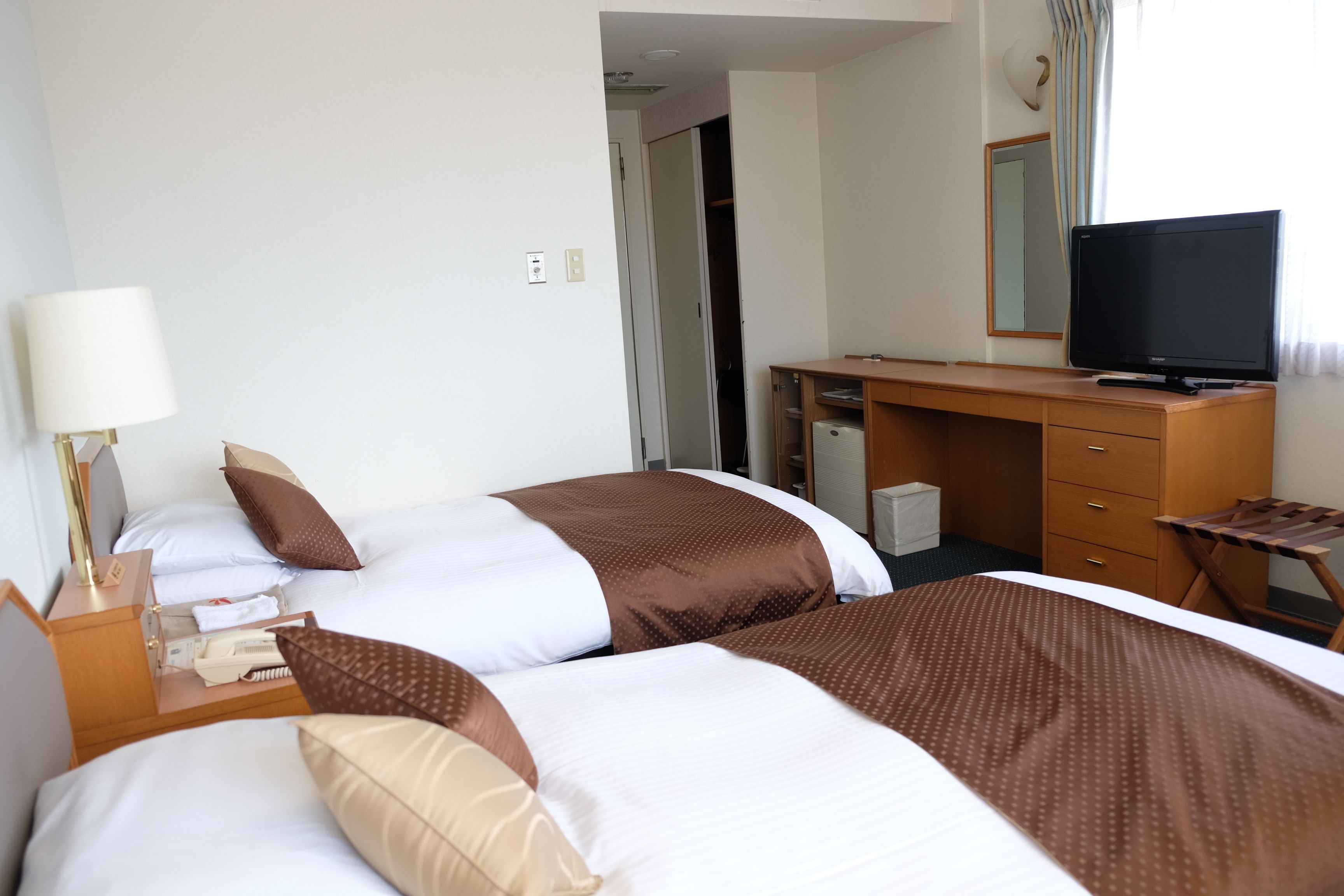 A hotel room with two beds, a desk, a television, and a mirror.