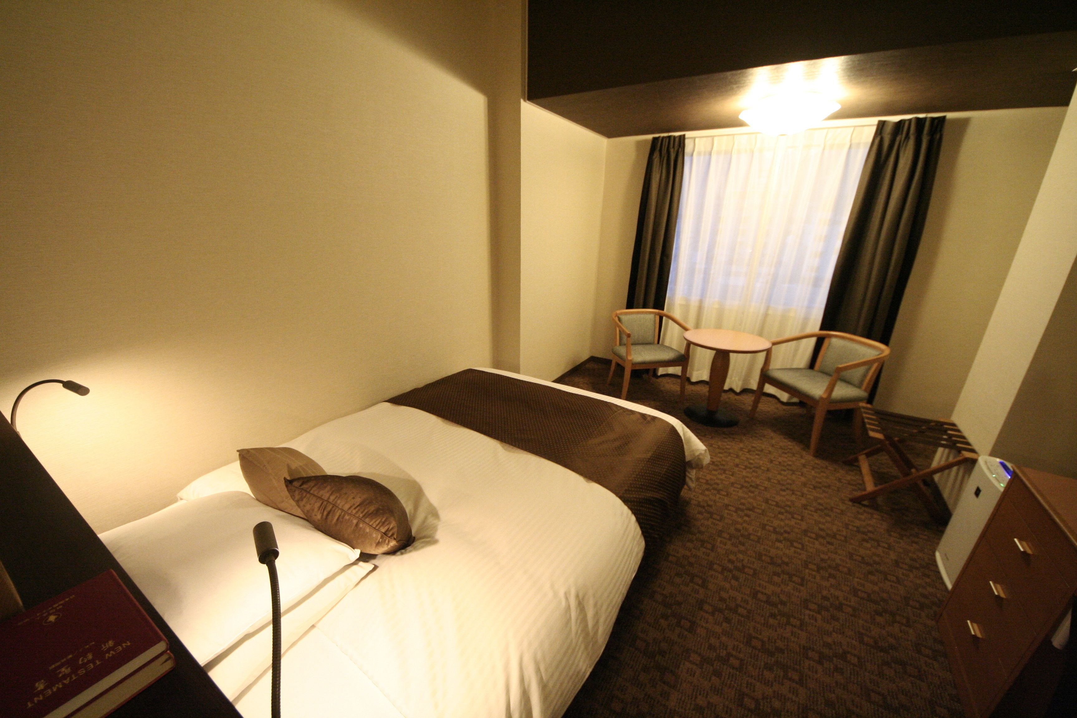 Una habitación de hotel con cama, escritorio, silla y lámpara.