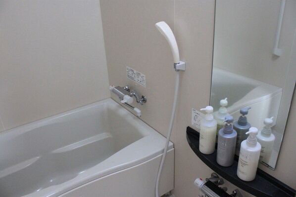 A bathroom with a bathtub, a shower, and a shelf with toiletries. - Hotel Uni Goten (Rishifuji)