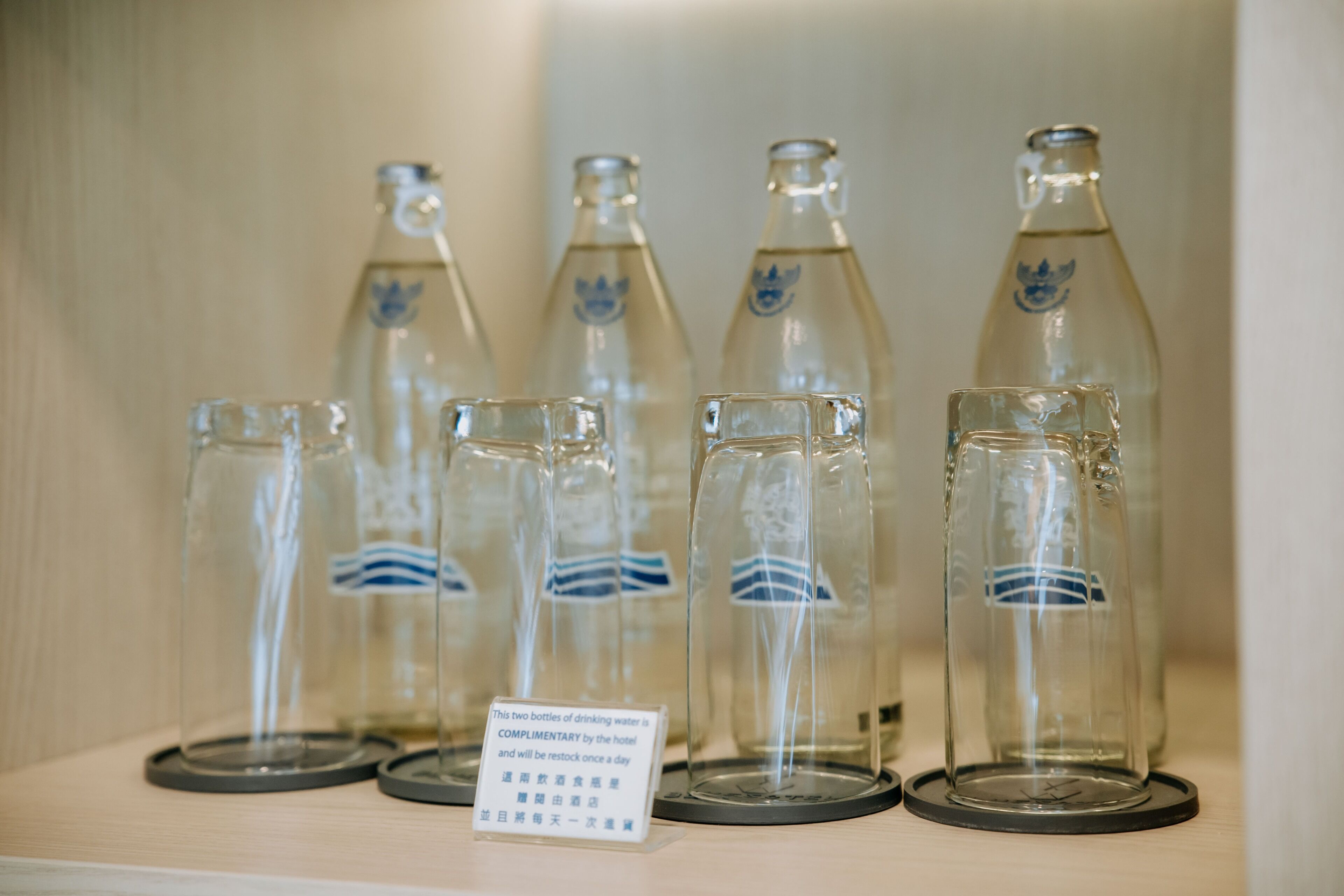 Une étagère présente une série de bouteilles en verre transparent, ornées de logos bleus.