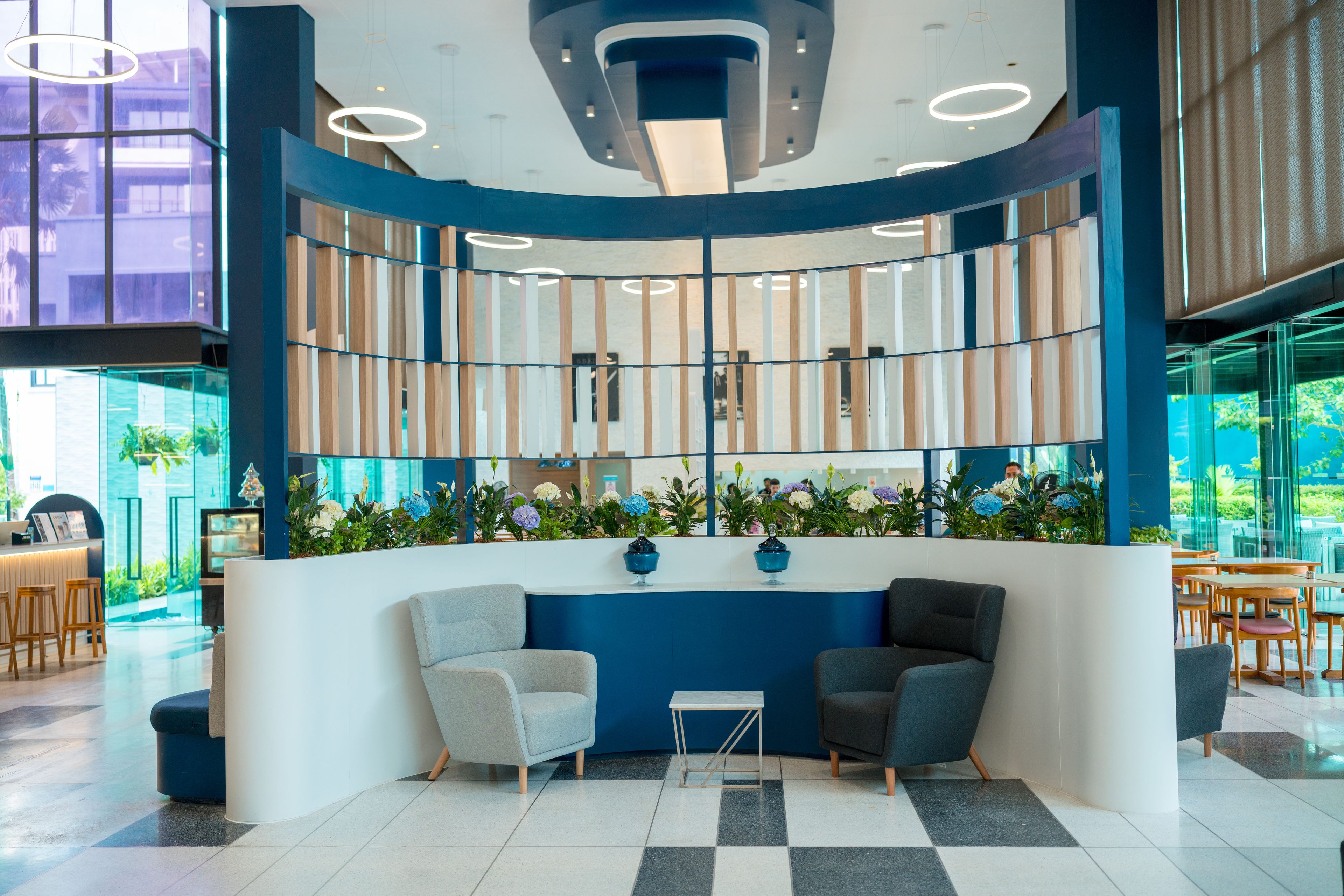 A reception area with a curved blue and white counter, two grey armchairs, a small table, and a floral arrangement.