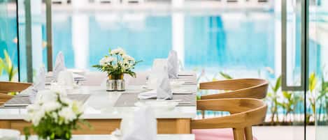 Mesa de comedor para dos, con vajilla blanca, un florero y vista a una piscina.