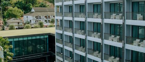 Un hotel moderno con piscina en la azotea, varios balcones y vistas a una exuberante ladera cubierta de vegetación.