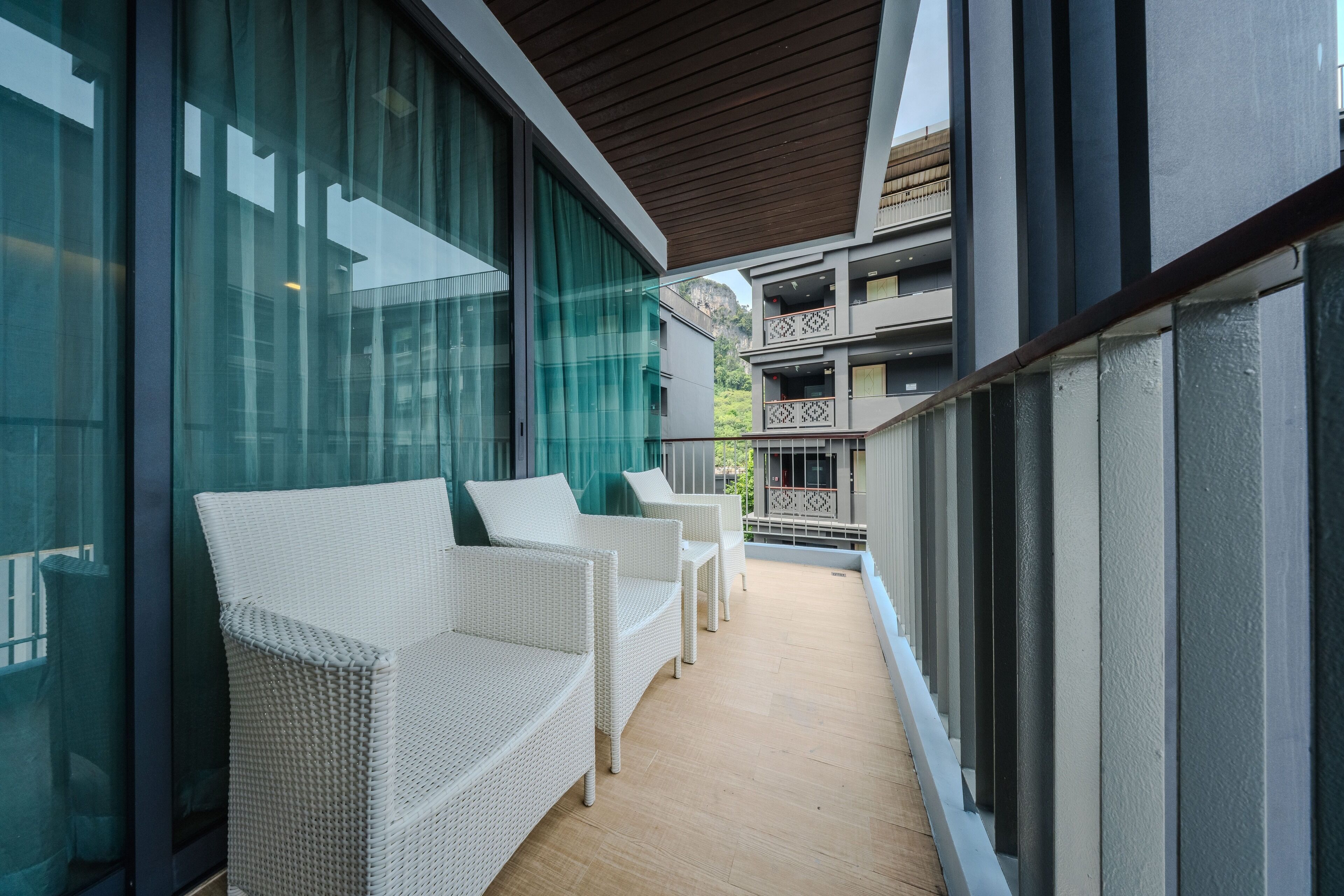 A balcony with white wicker furniture, large glass windows, and a view of a building with balconies.