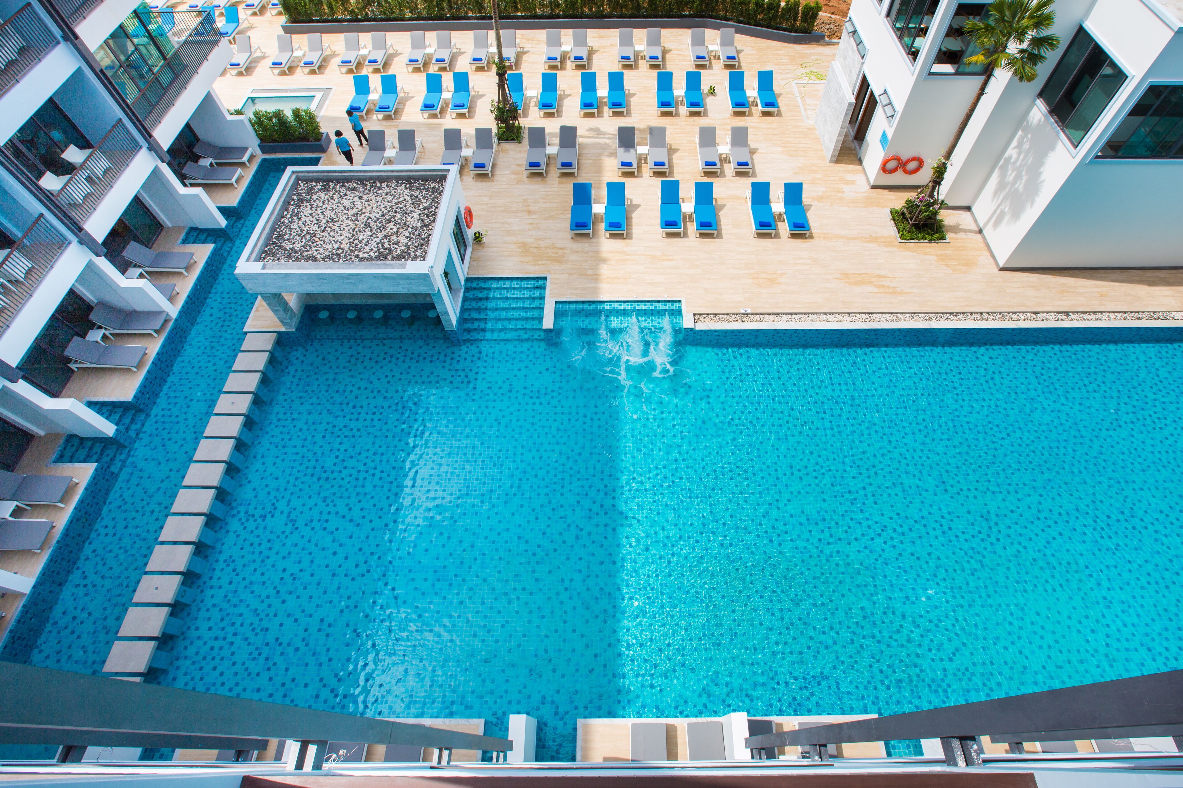 A rooftop pool with blue lounge chairs and a small waterfall feature.
