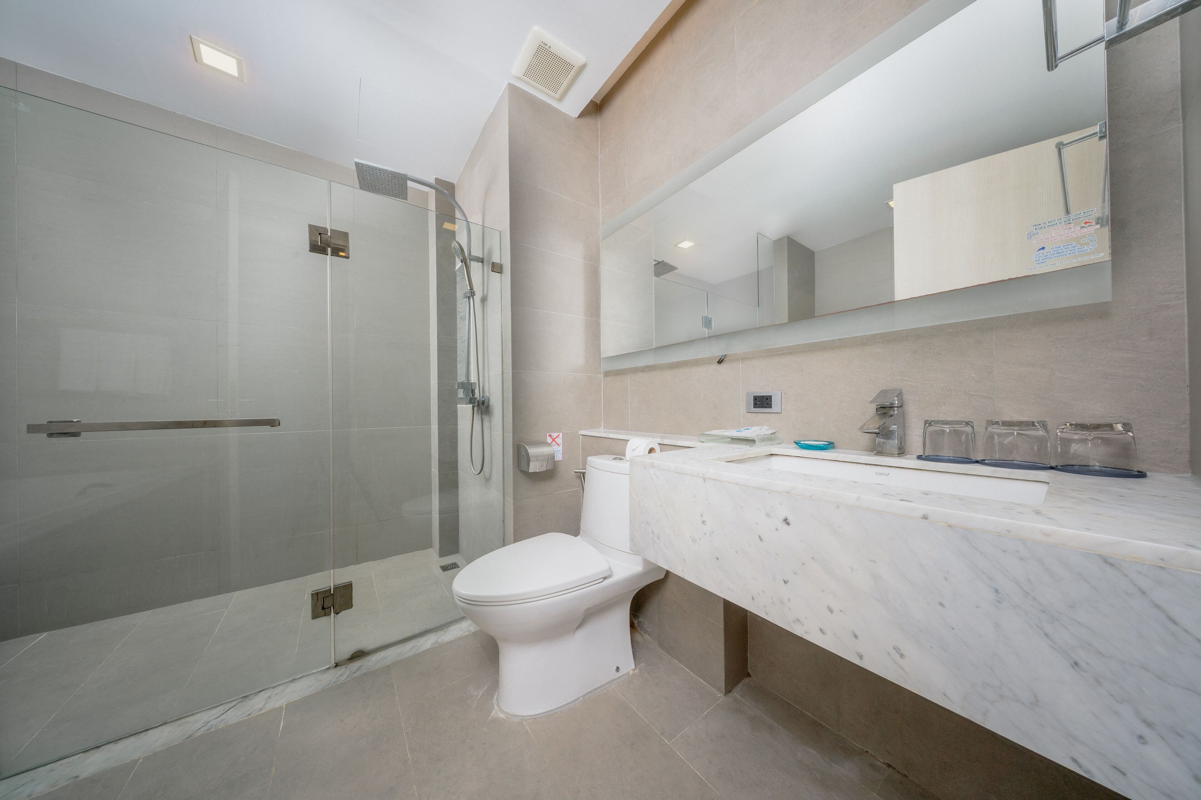 A modern bathroom with a glass shower enclosure, a white toilet, and a marble countertop with a mirror above.