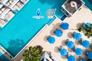 An aerial view of a hotel pool area with BlueSky Hotel and Green Hotel logos, multiple blue umbrellas, and sun loungers arranged on the poolside. - BlueSotel Krabi Ao Nang Beach (Krabi)