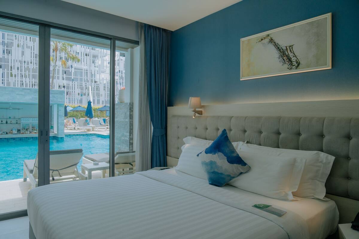 Une chambre d’hôtel avec un grand lit, une vue sur une piscine et un mur bleu.
