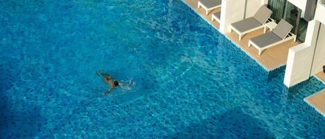 A swimming pool with clear blue water, surrounded by lounge chairs and a building with large windows.