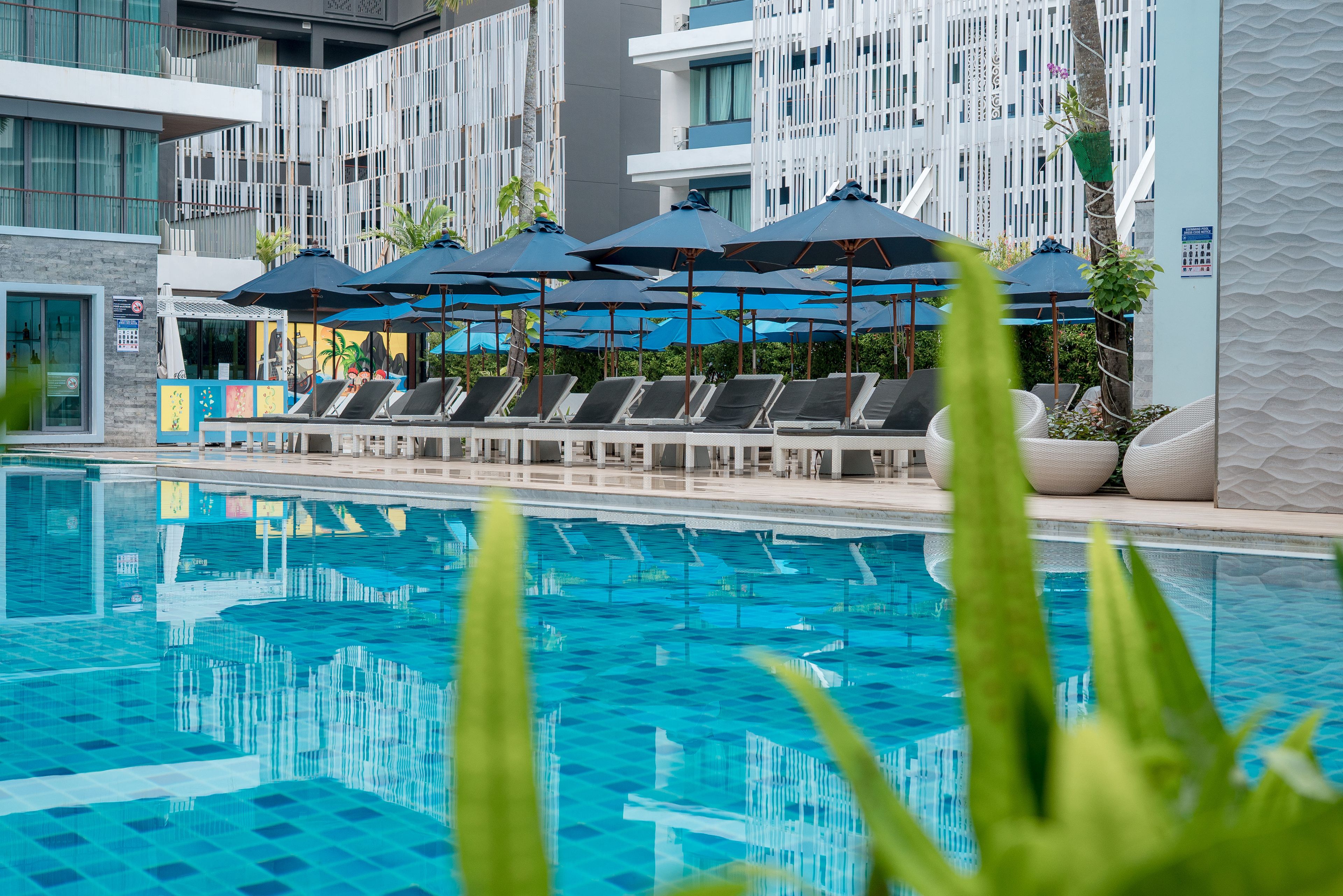 A swimming pool with lounge chairs and umbrellas, surrounded by modern buildings with balconies.