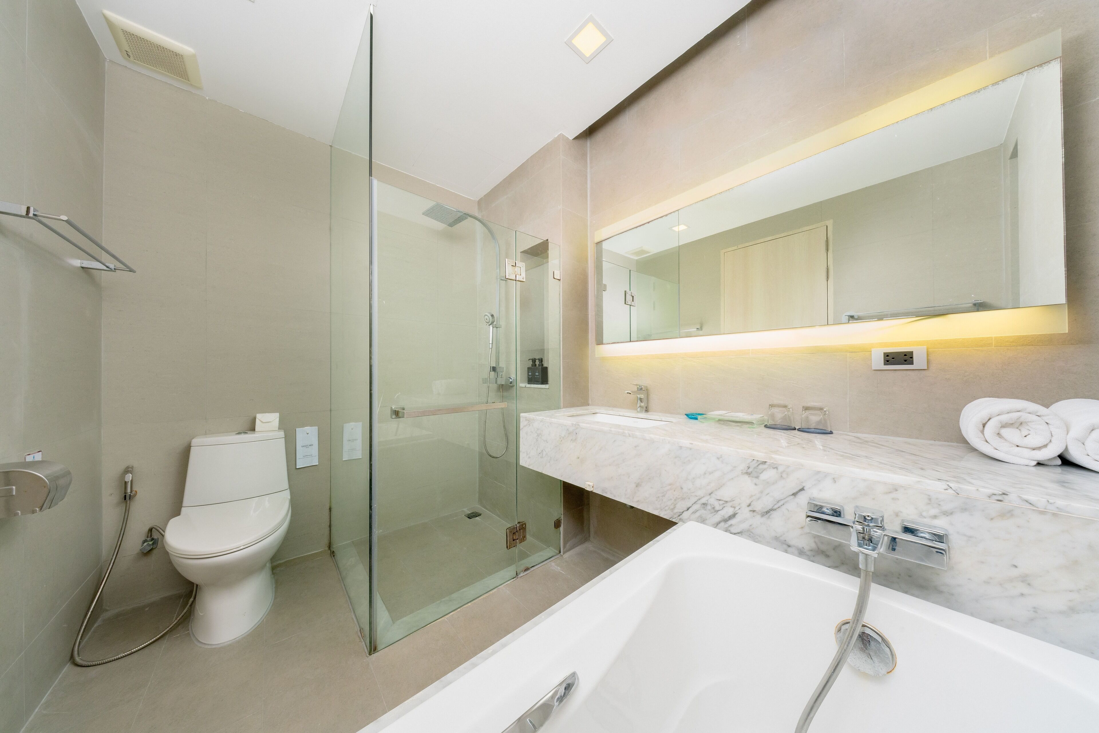 A modern bathroom with a glass-enclosed shower, a white toilet, a marble sink, and a large bathtub.