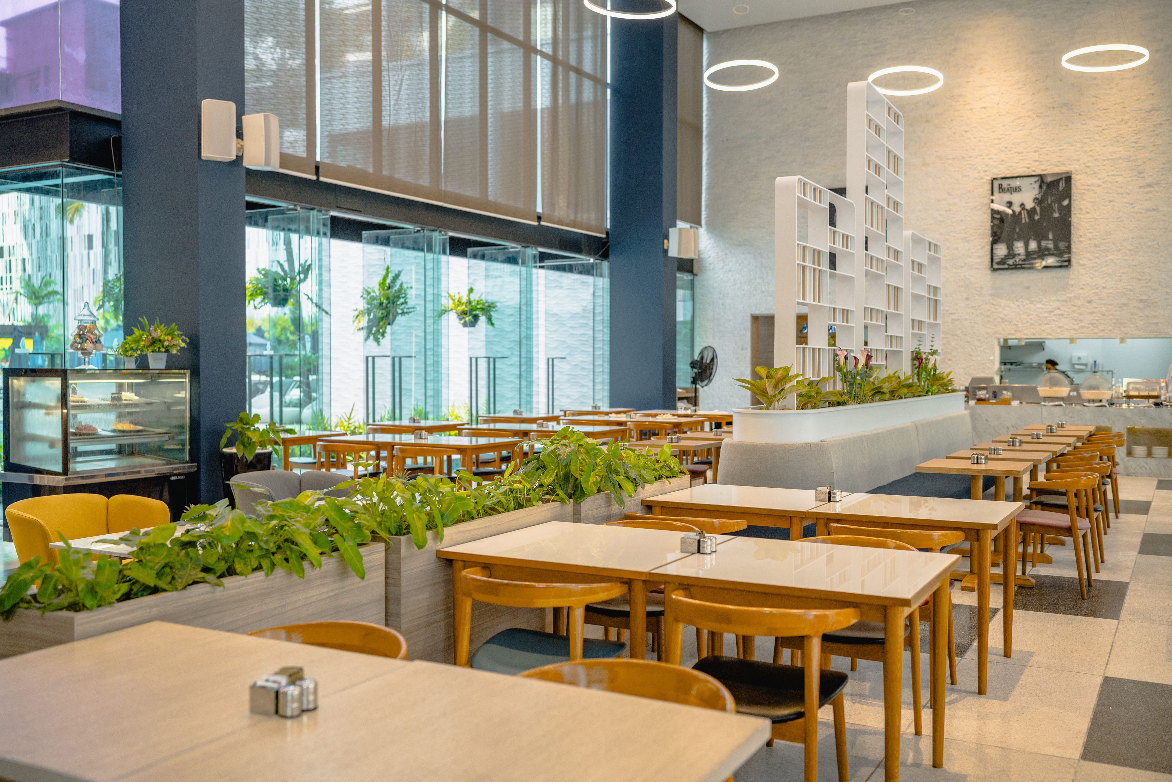 A modern restaurant with wooden tables and chairs, a glass display case, and a large window with plants.