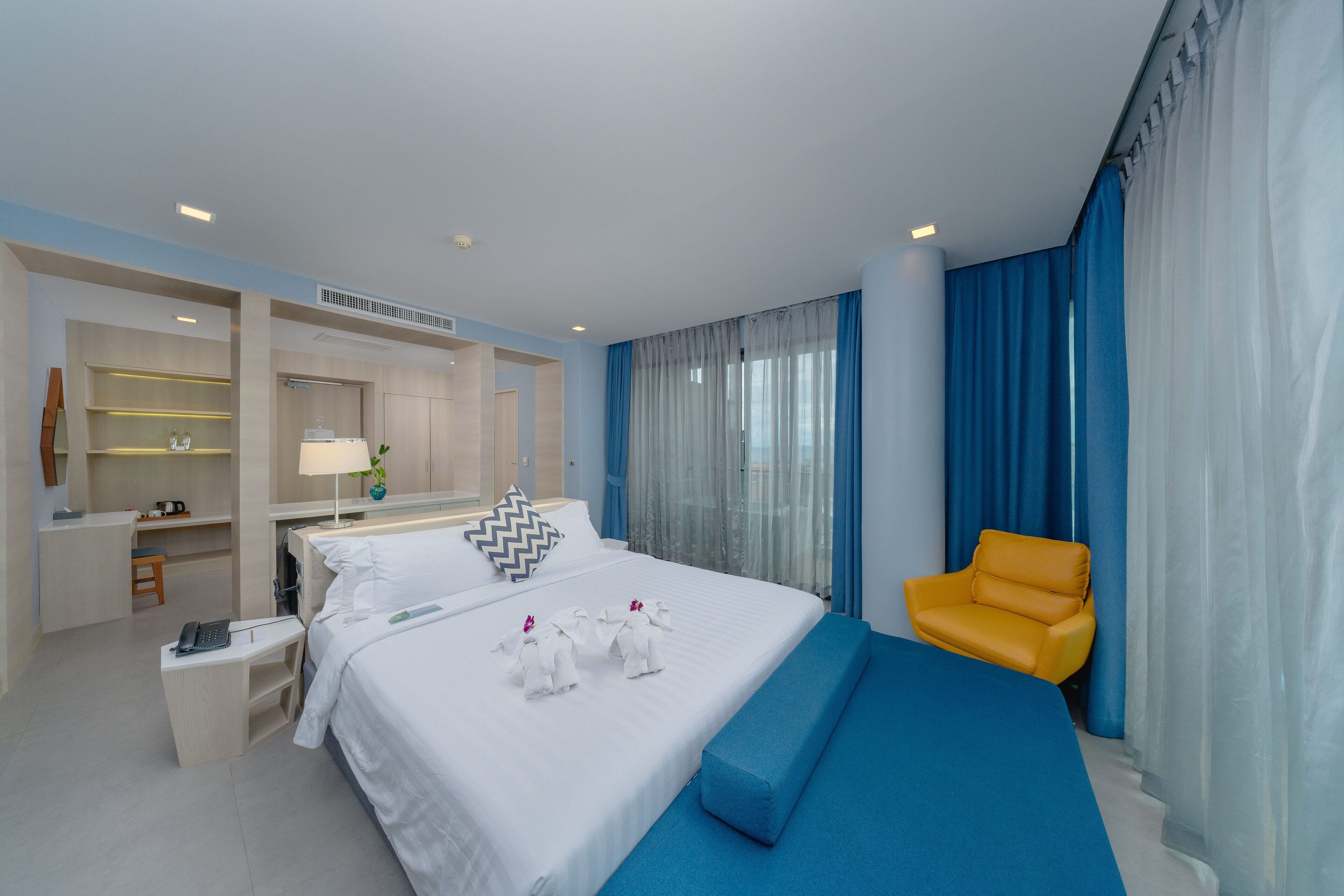 A hotel room with a large bed, a desk with a lamp, a chair, and a view of the outdoors.