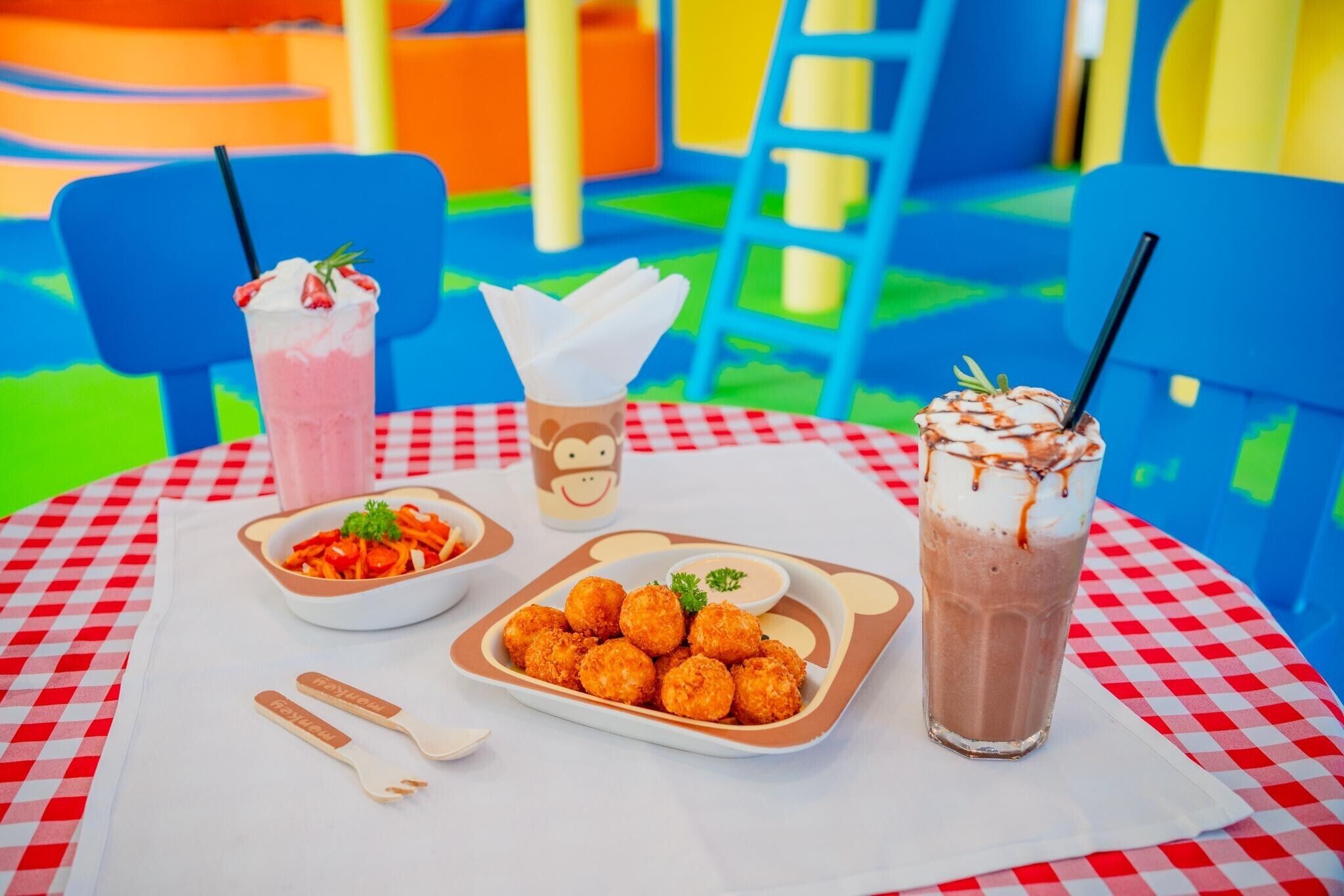 A table with a checkered tablecloth, a plate of fried food, a glass of iced drink, and a cup of hot chocolate.
