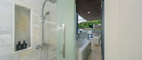 A modern bathroom with a glass-enclosed shower, marble walls, and a view of a balcony with outdoor furniture.