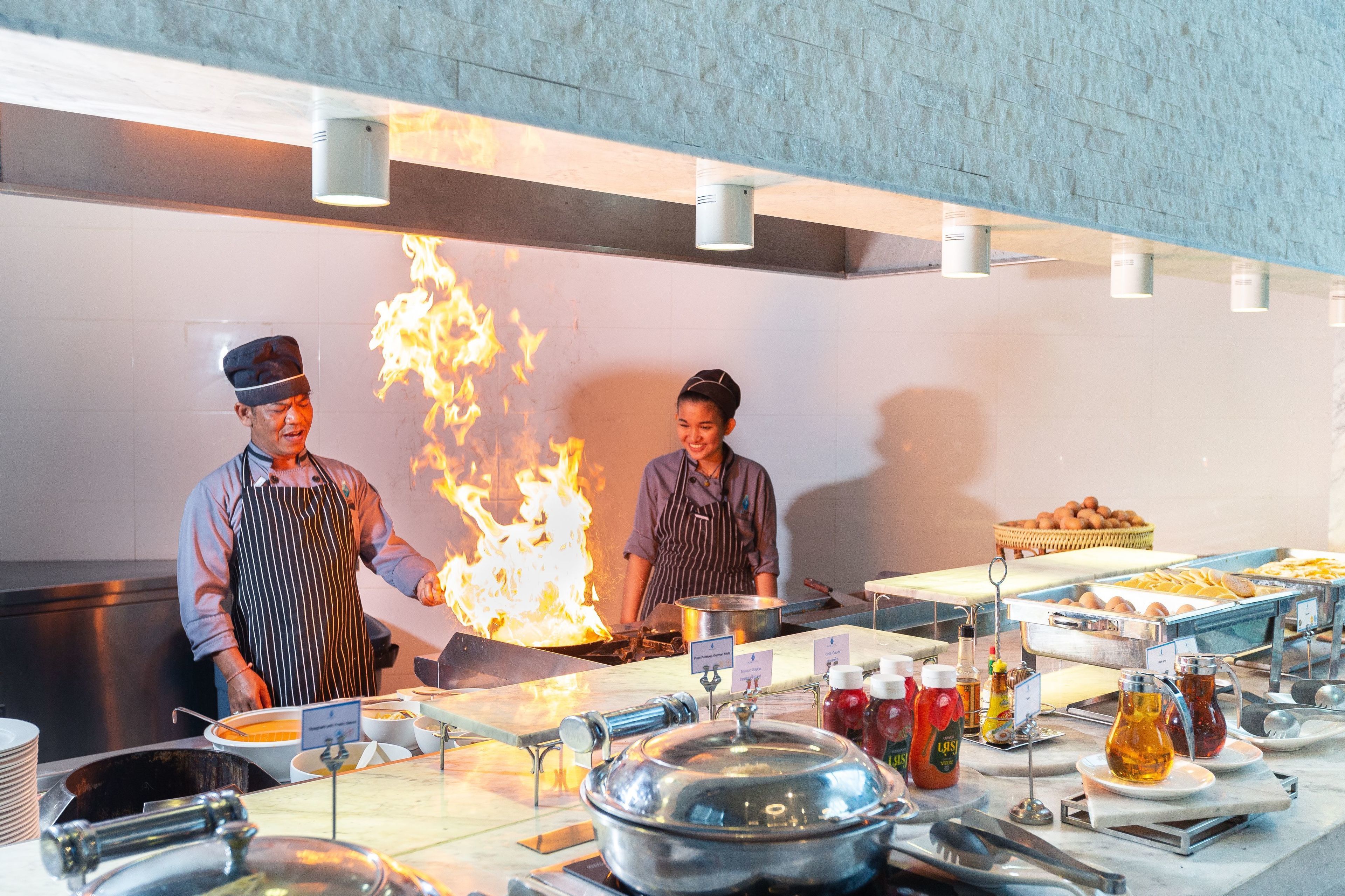 A commercial kitchen with chefs, a large fire, and various cooking equipment.