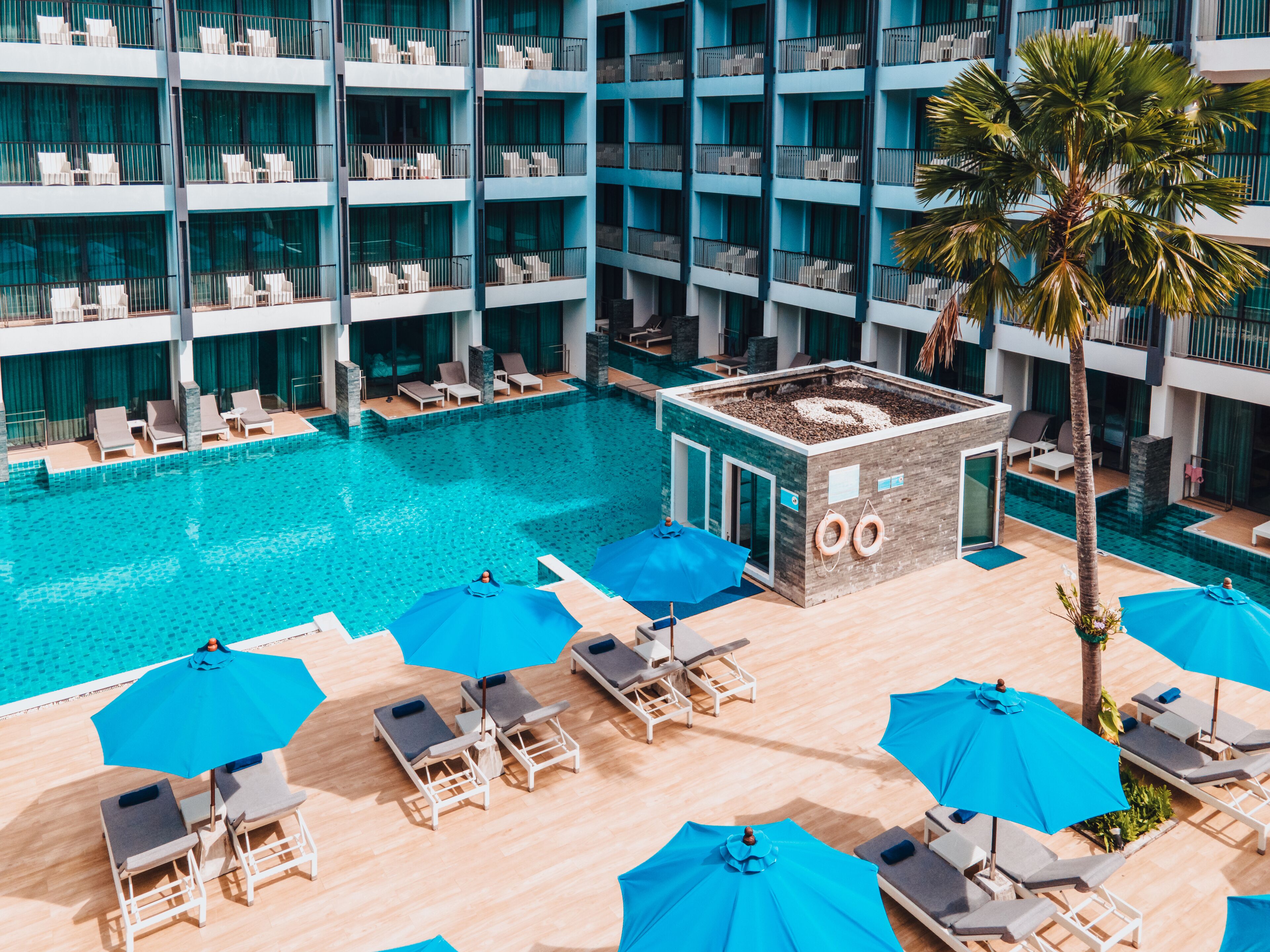 A hotel with multiple floors, a central swimming pool, and outdoor lounge areas with umbrellas.