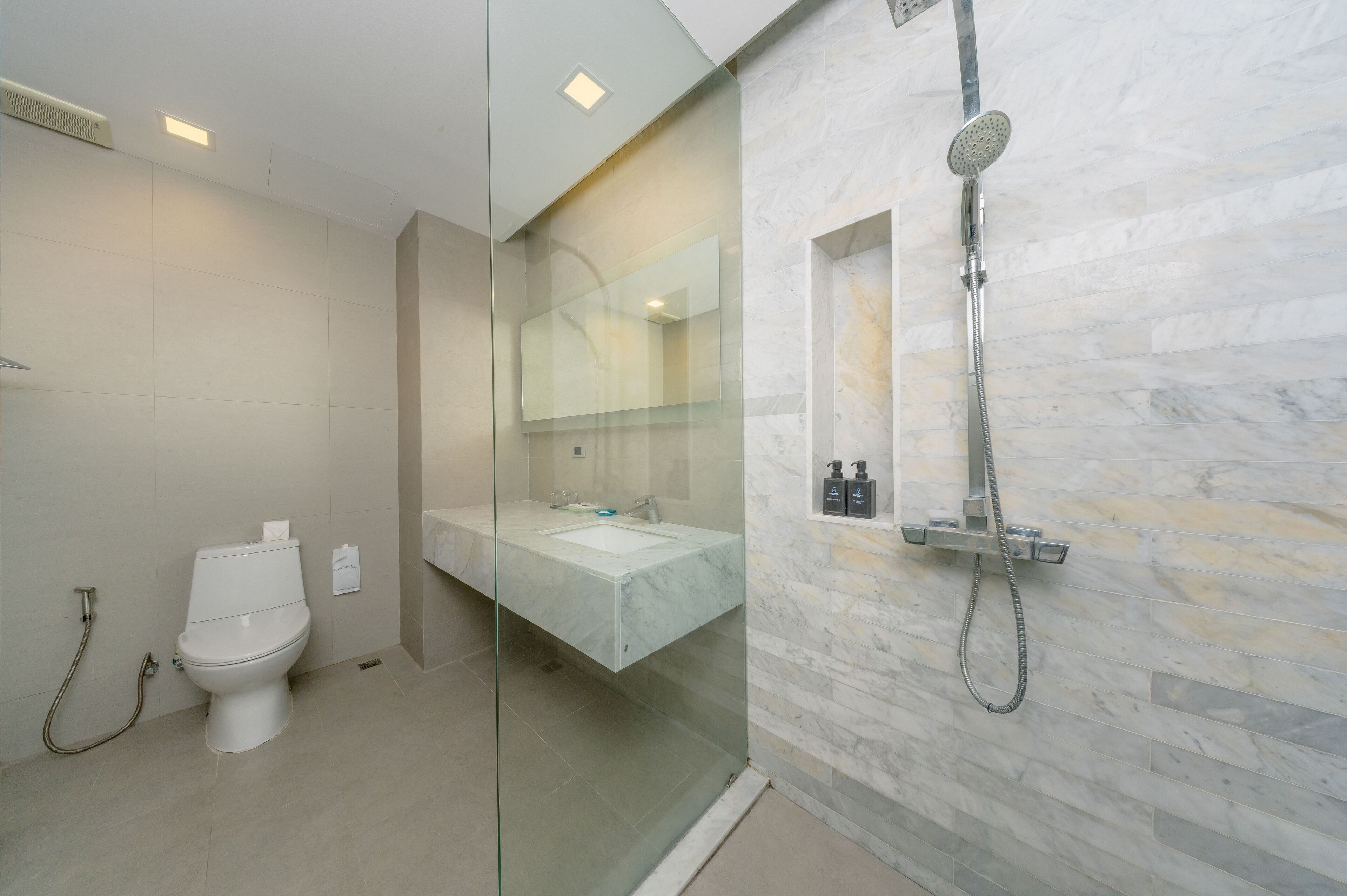 A modern bathroom with a glass-enclosed shower, a white toilet, and a marble-tiled wall.