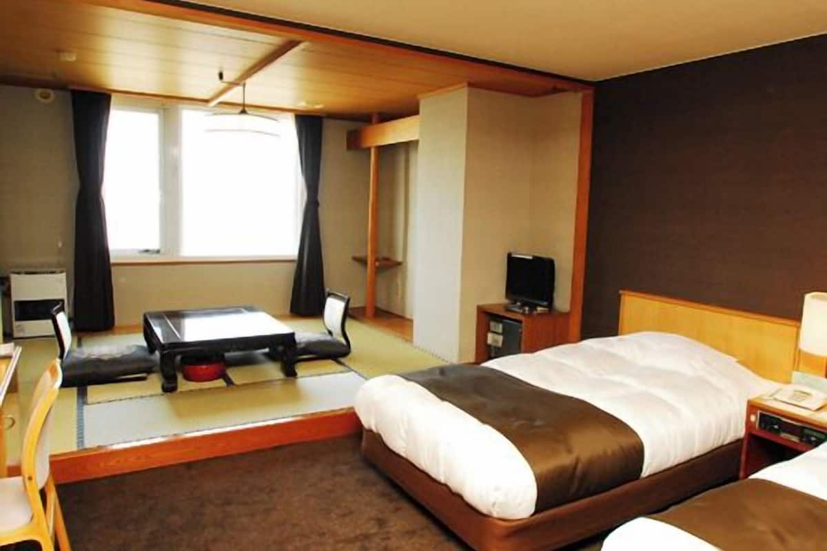 A hotel room with a bed, a desk, a chair, a television, and a window.
