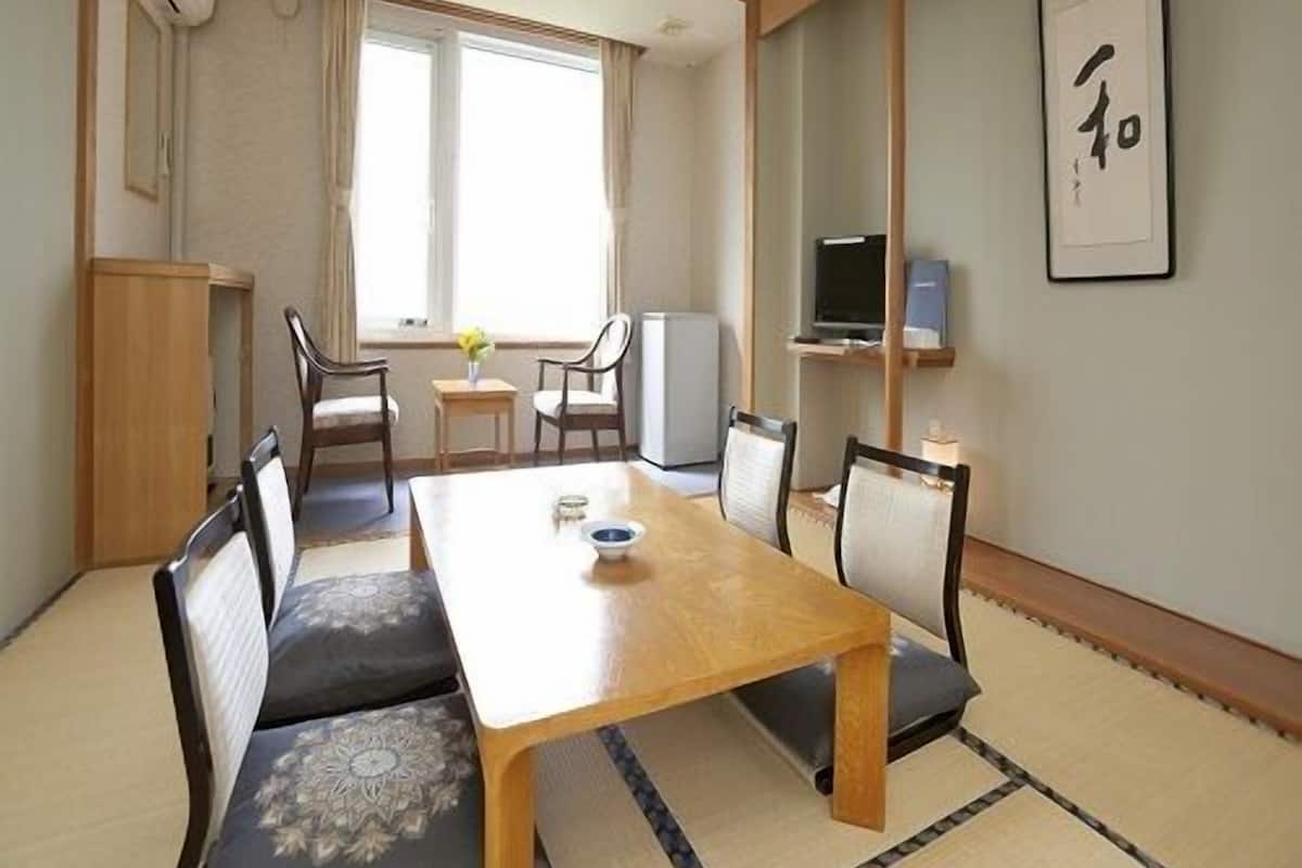 A traditional Japanese-style room with tatami flooring, a low table, and a TV on a shelf.