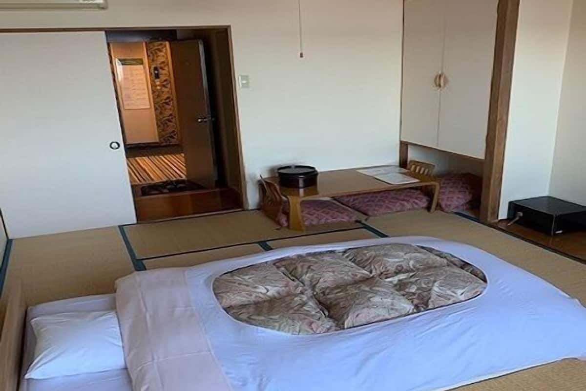 Quarto japonês tradicional com tatames, uma mesa baixa com almofada e uma cama com futon.